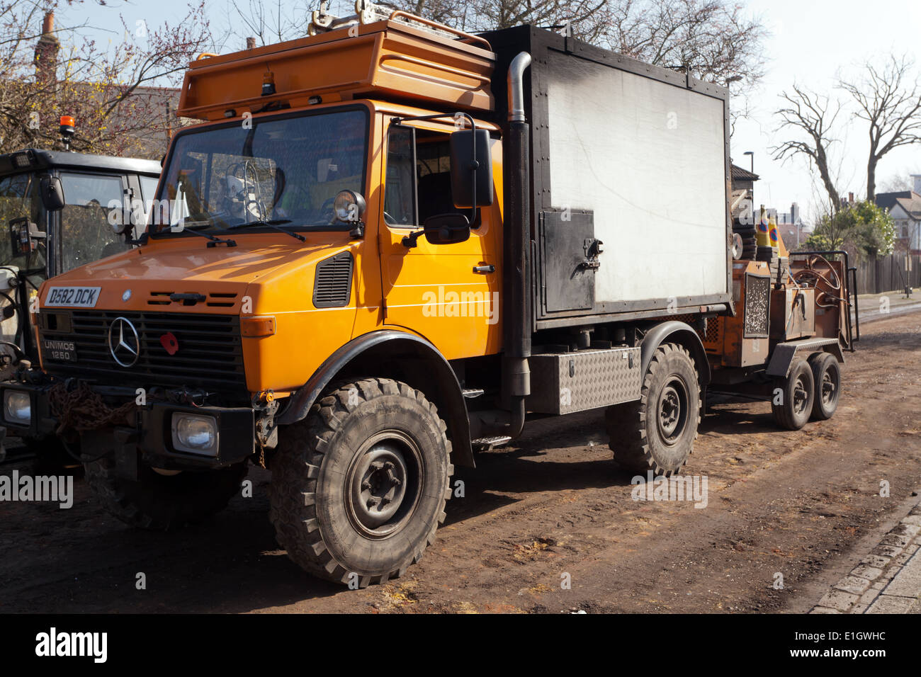 Dreiviertel Vorderansicht eines vierrädrigen Fahrzeugs Unimog 1250, das eine anhängermontierte Kappmaschine für die Baumoperation zieht. Stockfoto