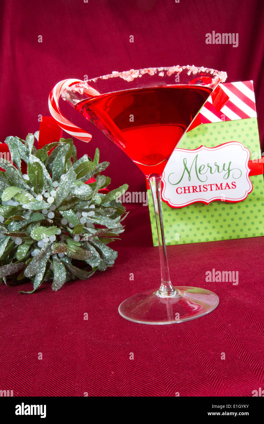 Martini-Glas umrandet mit zerquetschten Zuckerstangen gefüllt mit roter Flüssigkeit mit einer Geschenktüte Frohe Weihnachten und Mistel Stockfoto