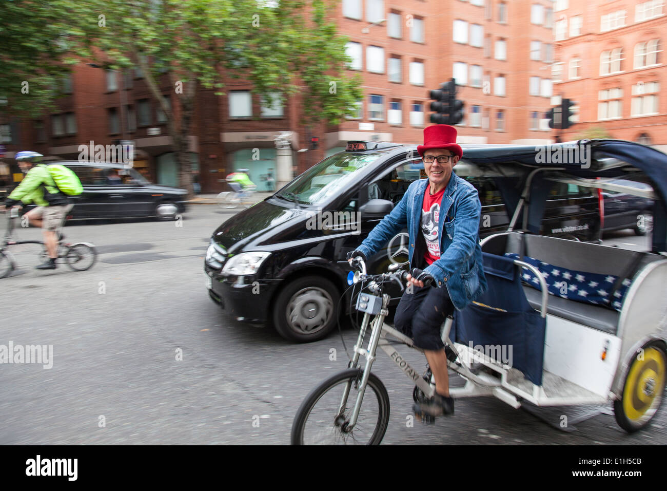 Ein Radfahrer trägt einen roten Hut, Lächeln, als er eine "Ecotaxi" oder "Fahrrad Rikscha" durch die belebten Straßen von London reitet Stockfoto