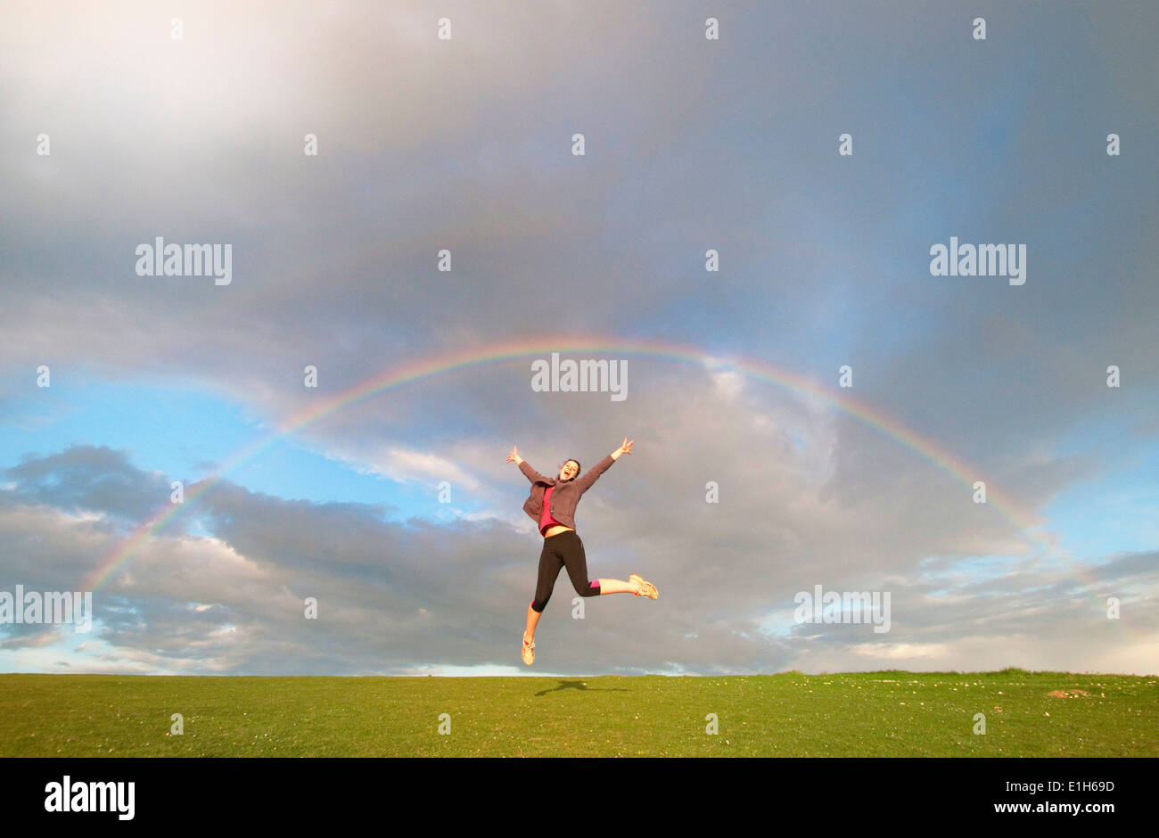 Junge weibliche Wanderer springen Luft unter Regenbogen Stockfoto