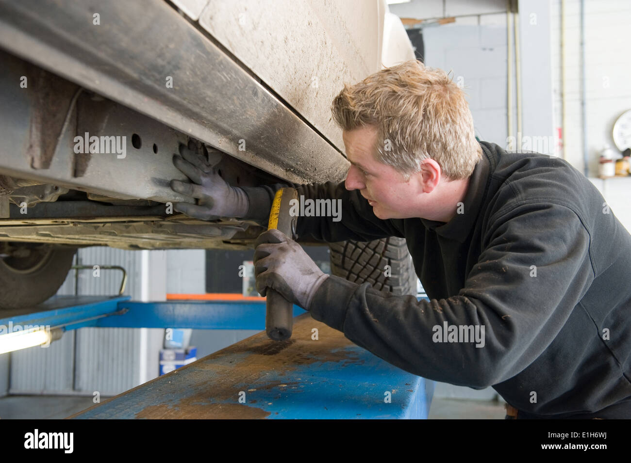 Ein Mechaniker prüft die Fahrgestell-Nummer von einem angehobenen Auto auf einer Brücke in einer Garage. Stockfoto