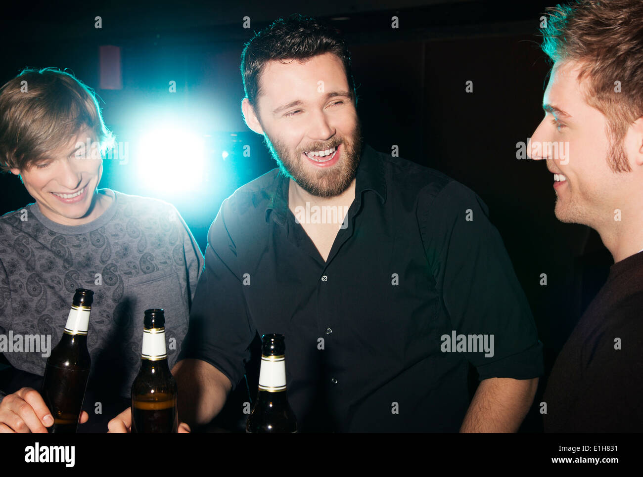 Drei männliche Freunde trinken Flaschenbier in Nachtclub Stockfoto
