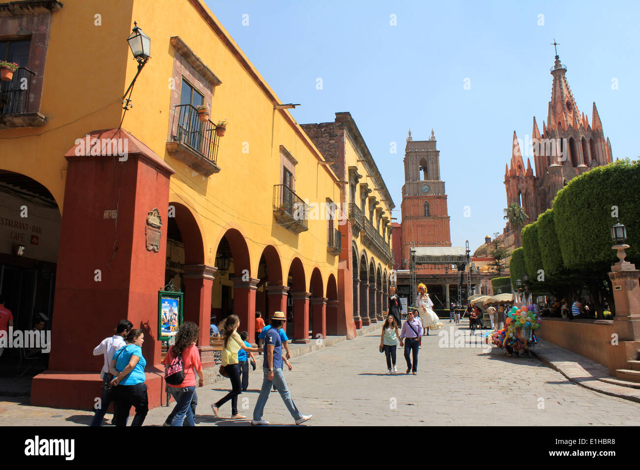 Arcaded Gebäude und Kirchen auf dem Hauptplatz mit Fußgängern durch den zentralen Park n San Miguel de Allende, Guanajuato, Mexiko Stockfoto