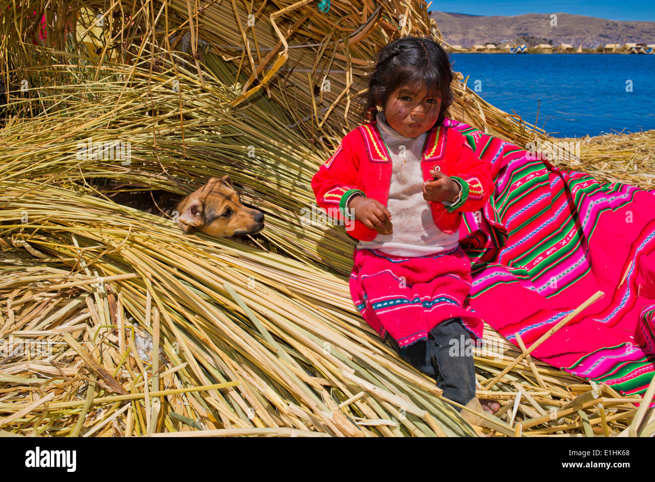 Junges Mädchen der Uro-Indianer, ca. 5 Jahre alt, tragen traditionelle Kleidung, sitzt neben einem Hund Schilf Bündel, schwimmende Stockfoto