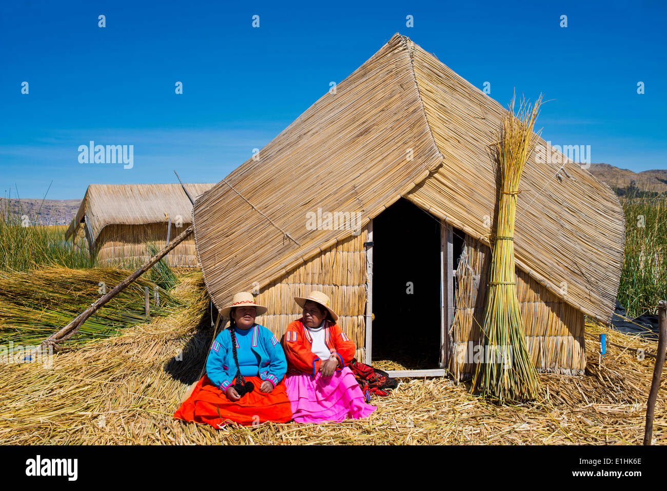 Zwei Frauen der Uro-Indianer tragen traditionelle Kleidung sitzt vor einem Reed-Hütte gemacht schwimmenden Inseln von Totora-Schilf Stockfoto