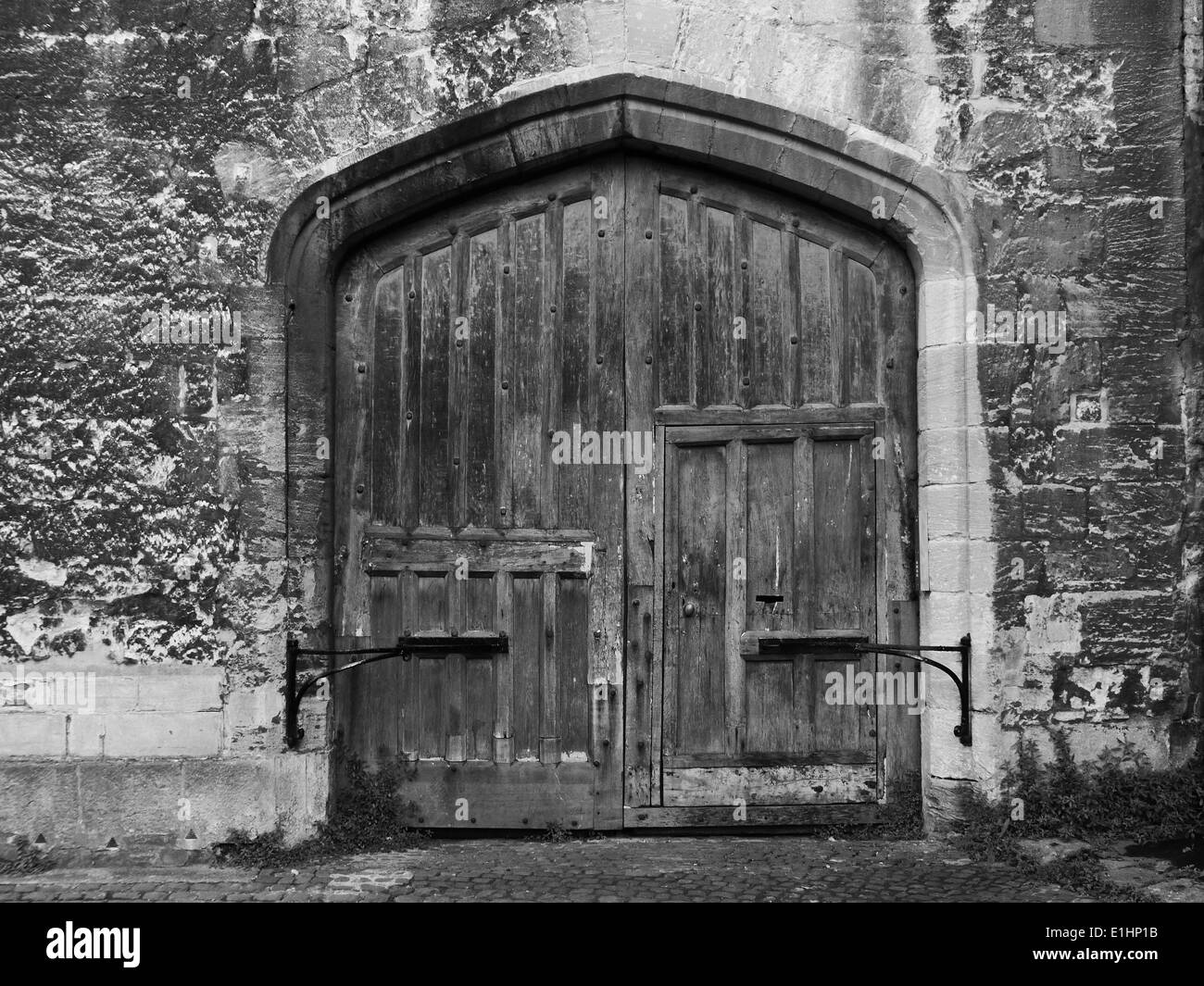 Eine alte hölzerne Doppeltür gesetzt in eine Steinmauer in schwarz / weiß Stockfoto