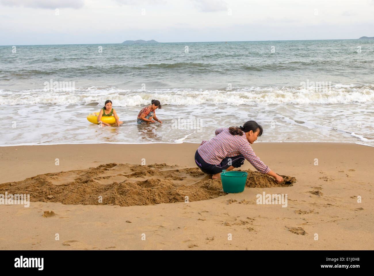 Eine Frau, die nahe der Küste lebenden Muscheln am Strand Graben ist. Stockfoto