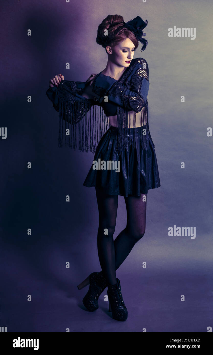 Frau trägt schwarze Kleidung und kleine Zylinder stand vor lila Hintergrund Stockfoto