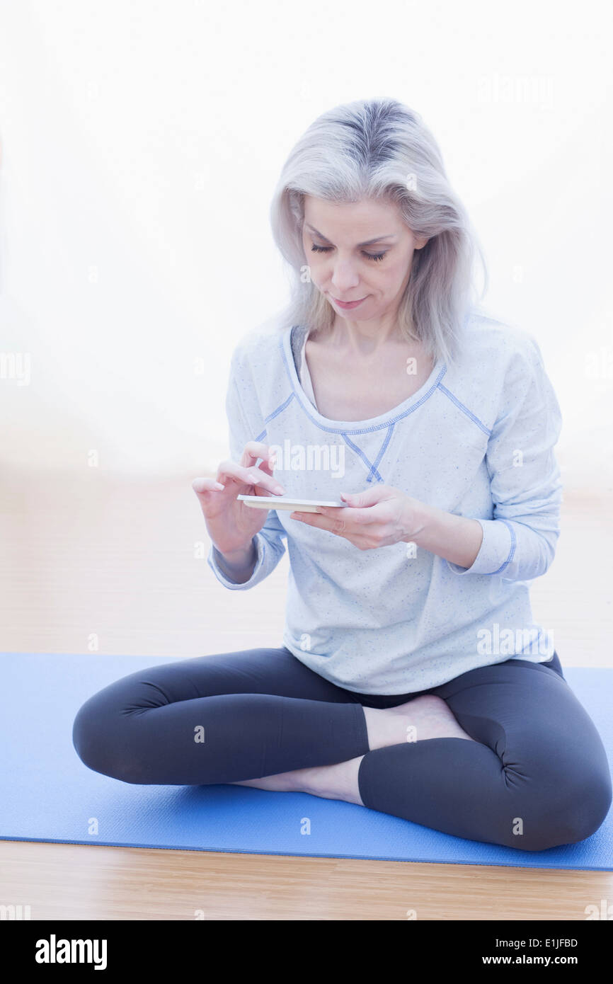 Reife Frau in Lotus-Pose, mit Mobiltelefon Stockfoto