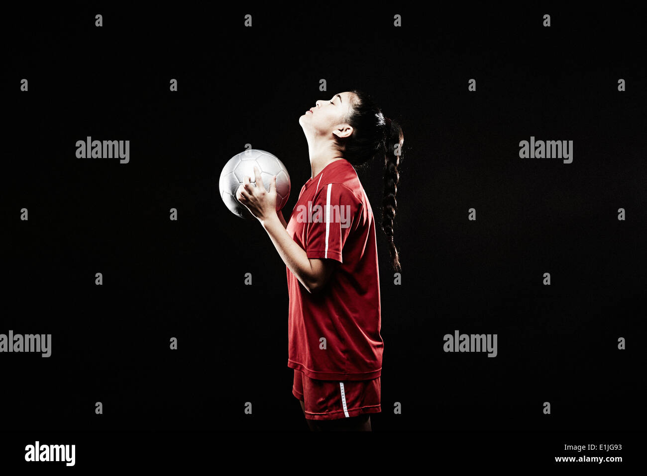 Junge Frau hält Fußball, Blick nach oben Stockfoto