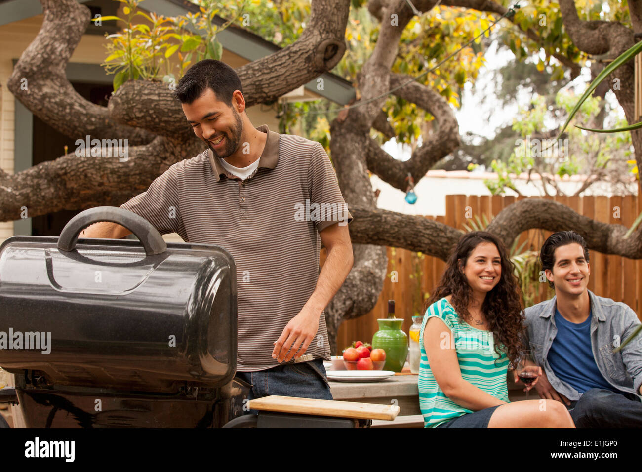 Mann, Kochen am Grill, Freunde im Hintergrund Stockfoto