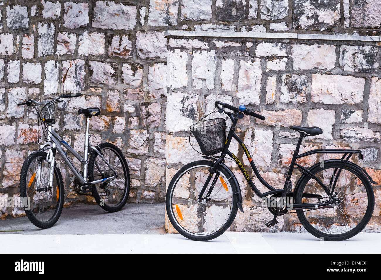 zwei Fahrräder werden gezeigt, eine Wand in Vis Insel Kroatien gelehnt. das Schwarz der Bikes kontrastiert gegen den Stein Stockfoto