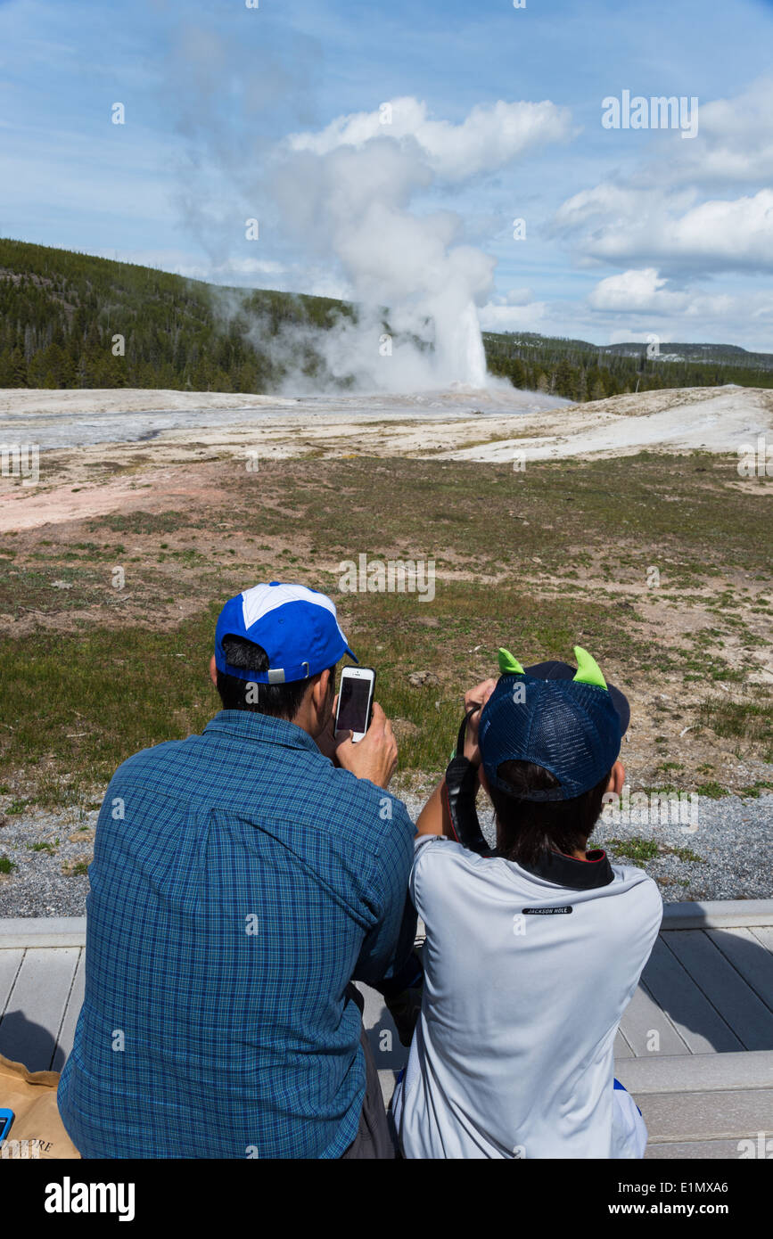 Vater und Sohn machen Handy Fotos von Old Faithful Geysir Ausbruch. Yellowstone-Nationalpark, Wyoming, USA. Stockfoto