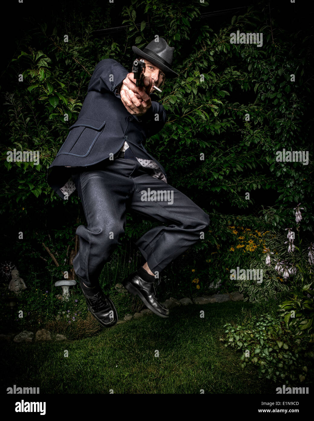 Ein Mann in einem Vintage-Stil-Anzug gekleidet und mit dem Ziel einer Pistole beim Springen in der Luft. Stockfoto