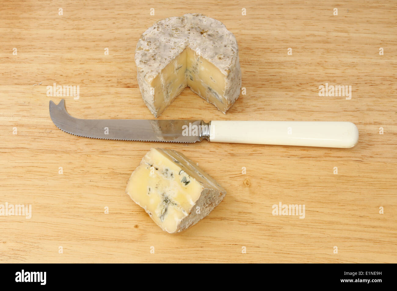 Runde der Blauschimmelkäse mit einem Stück ausgeschnitten und ein Käsemesser auf einem Holzbrett Stockfoto