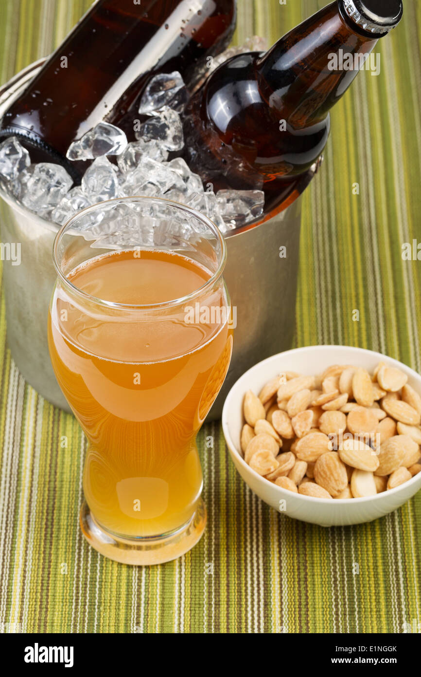 Closeup vertikale Foto von einem goldenen Bier in Longdrinkglas mit gesalzenen Nüssen in Schälchen mit Flaschenbier in Eimer mit Eis Stockfoto