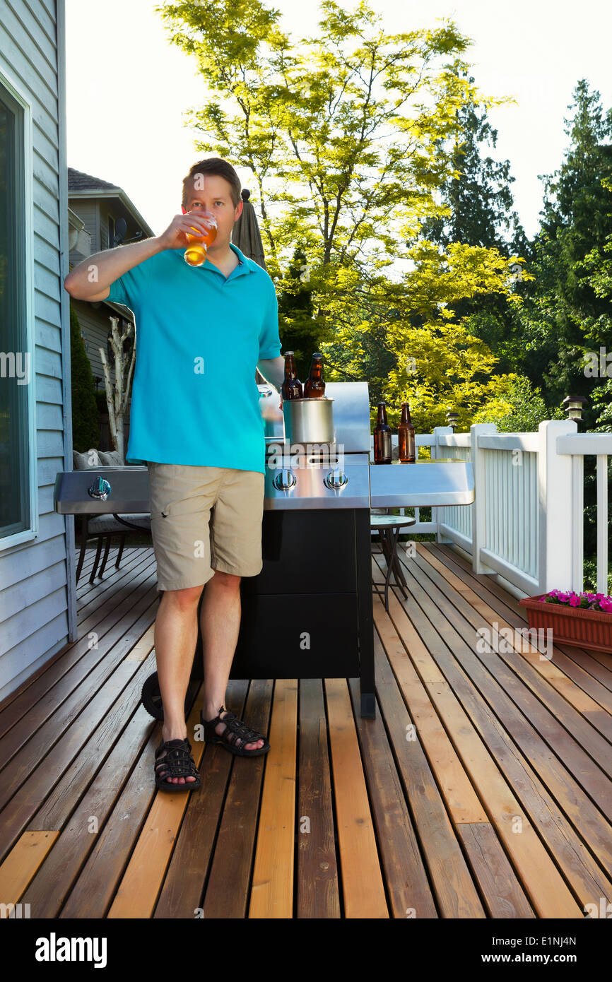 Foto von reifer Mann Bier zu trinken, während der Vorbereitung auf Outdoor-Zeder Holz Terrasse grillen Stockfoto