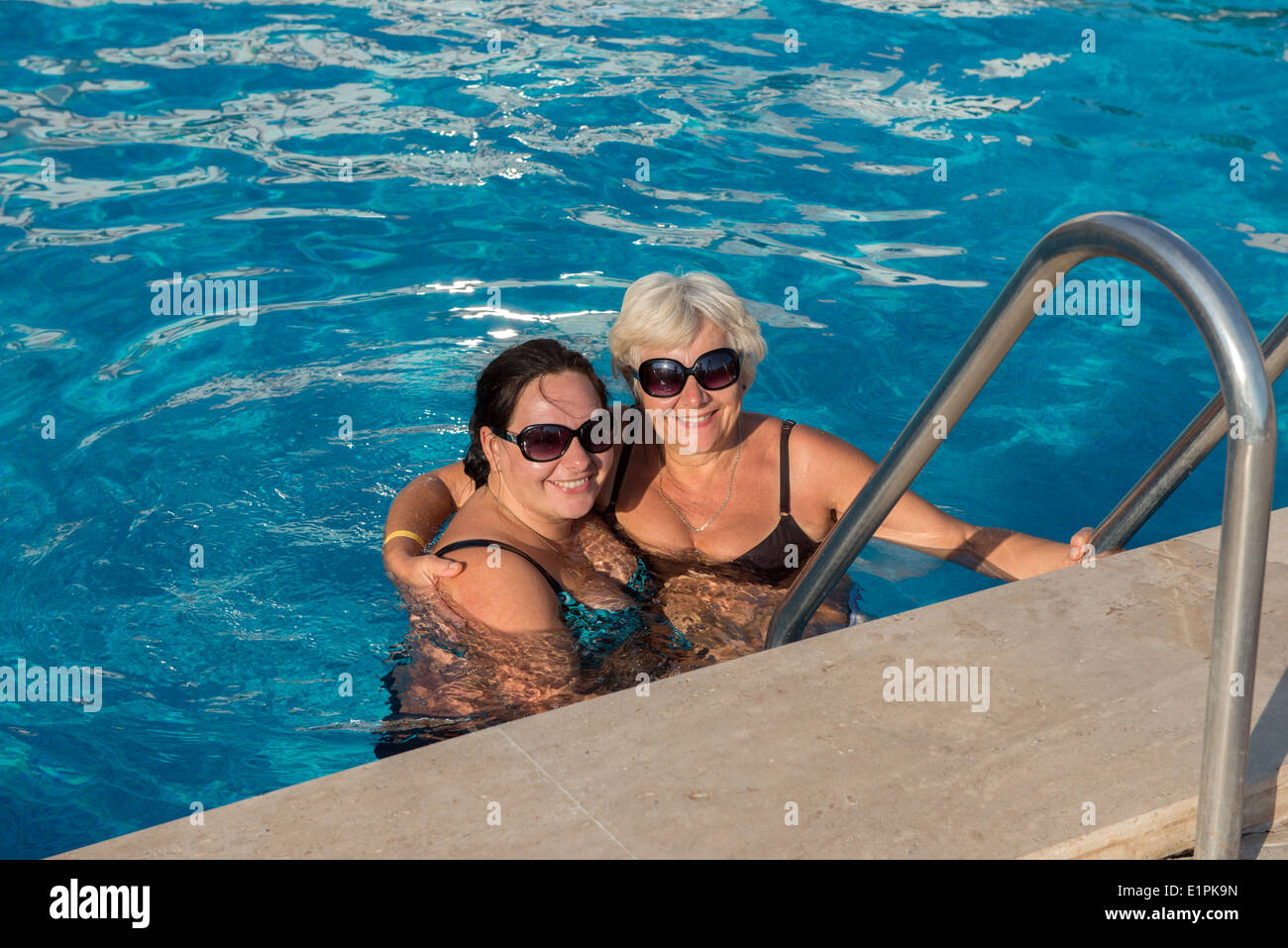 Mutter mit Liebe umarmt ihre Tochter im Wasser am Rande eines Swimmingpools. Stockfoto