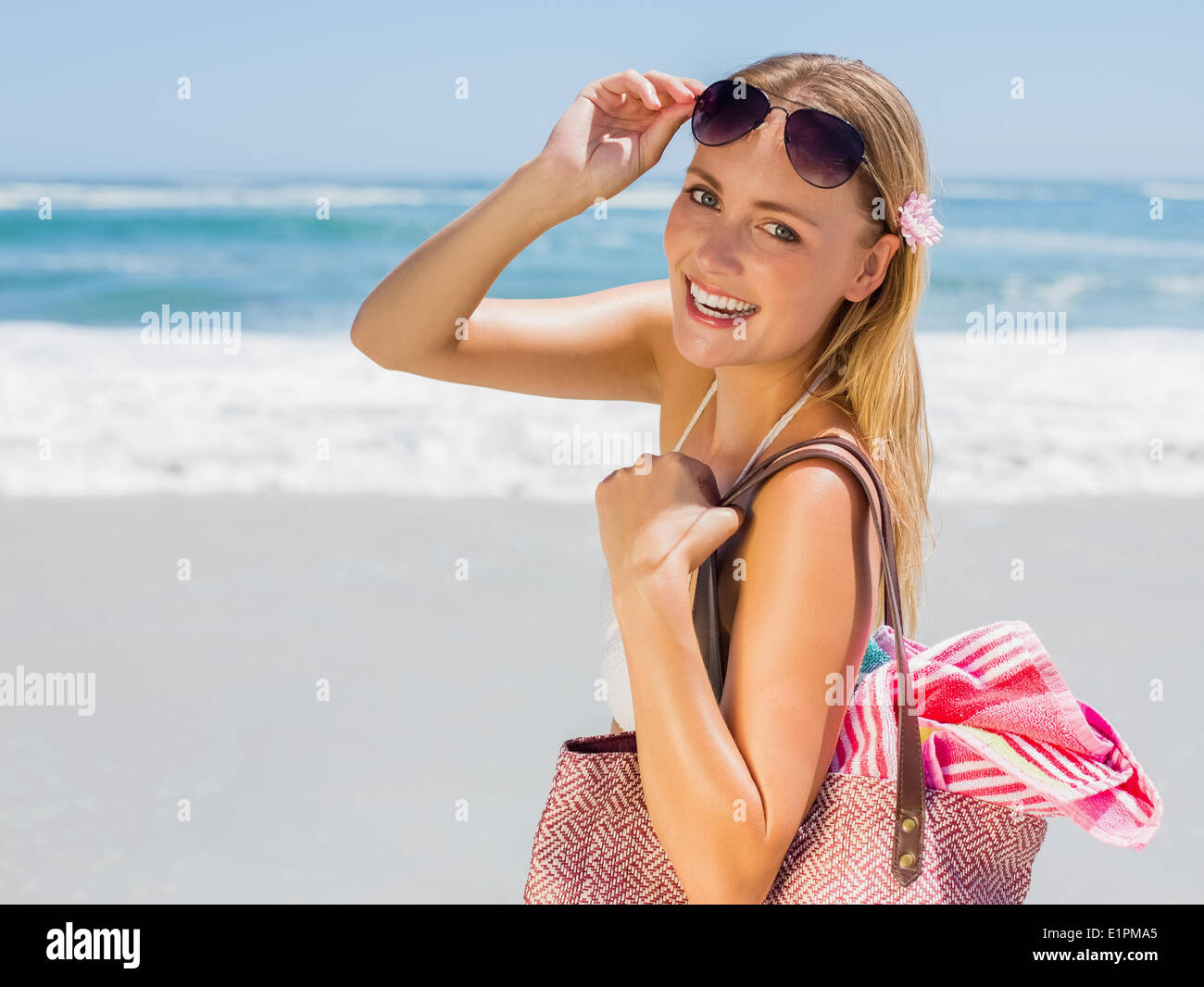 Lächelnde Blondine Tragetasche und Handtuch am Strand Stockfoto