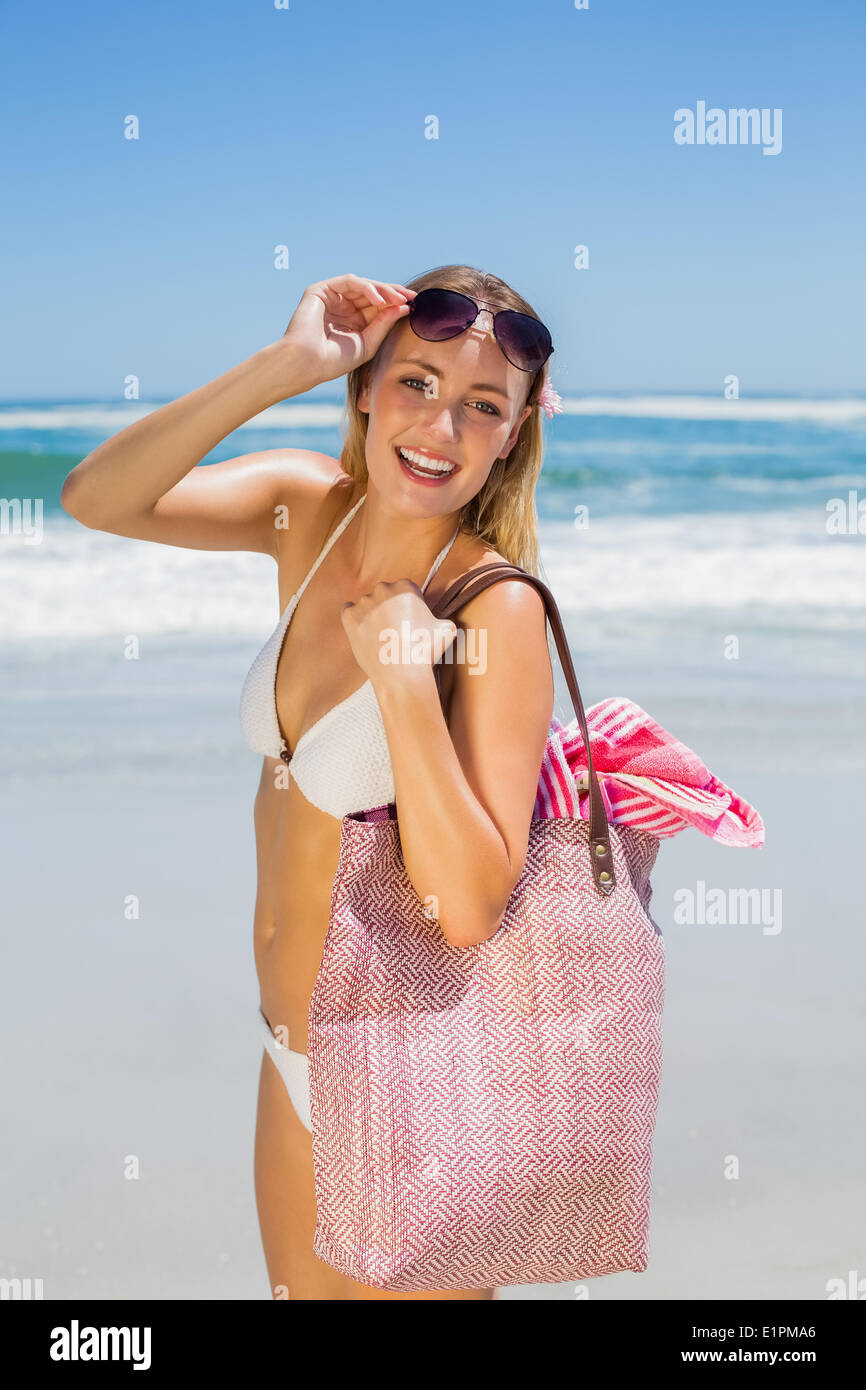 Lächelnde Blondine Tragetasche und Handtuch am Strand Stockfoto