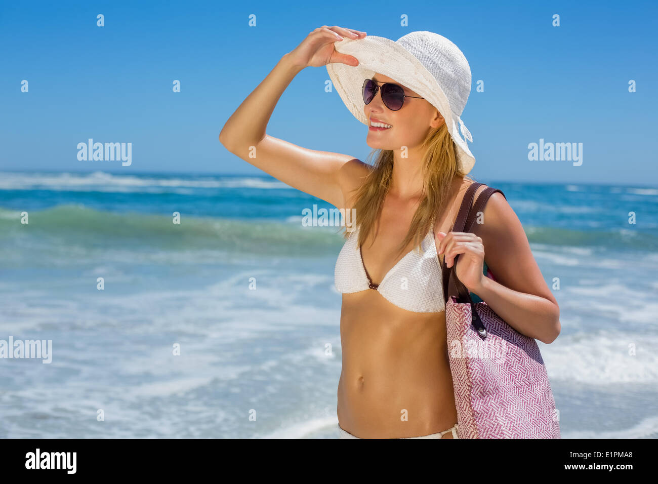Lächelnde Blondine im weißen Bikini Tragetasche am Strand Stockfoto