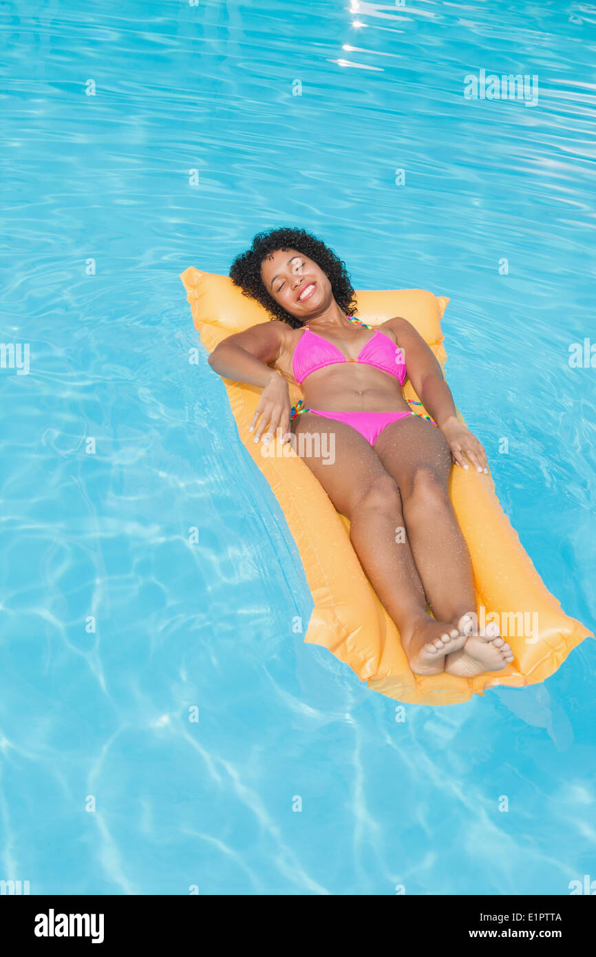 Lächelnde Frau in rosa Bikini liegen auf Lilo im Schwimmbad Stockfoto