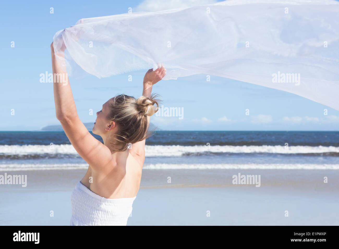 Hübsche Blondine hält weißen Schal am Strand Stockfoto