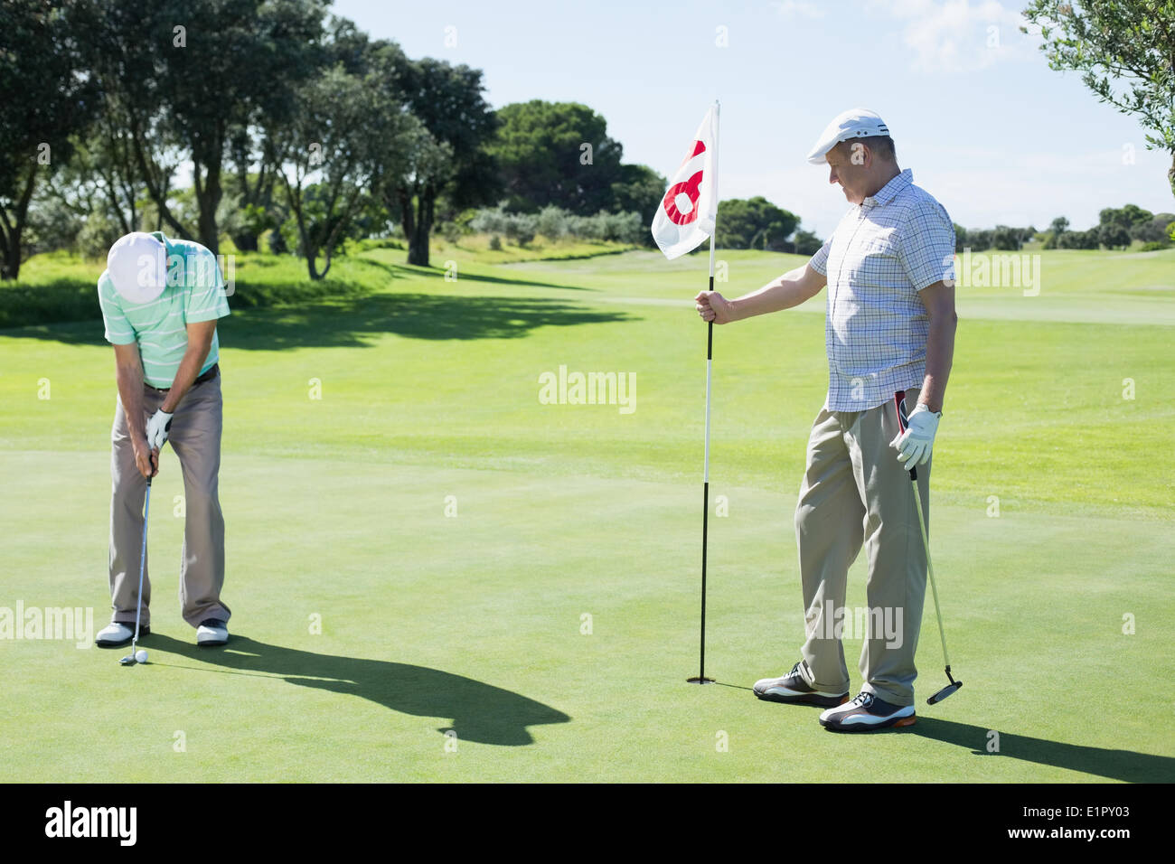 Golfer halten achtzehnten Loch Flagge für Freund setzen Kugel Stockfoto