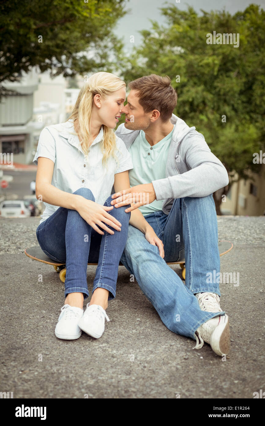 Hip junges Paar sitzt auf Skateboard küssen Stockfoto