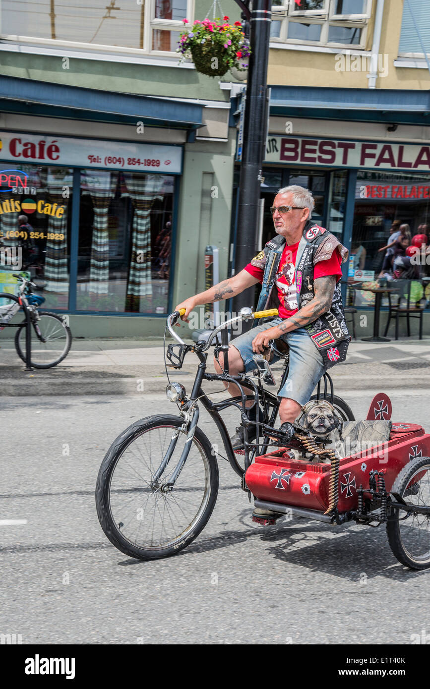 Mann auf dem Fahrrad (Multi-Media Künstler Mad Dog) mit Punk-Beiwagen mit Maschinengewehr und behelmter Hund Stockfoto