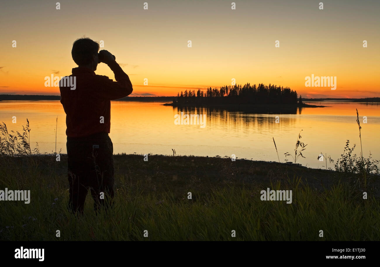 Mittleren Alters männlichen Wanderer Blick auf Astotin Lake mit dem Fernglas in der Abenddämmerung, Elk Island Park, Alberta, Kanada. Stockfoto