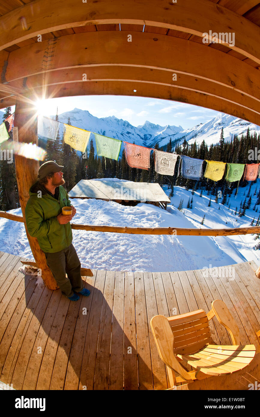 Ein Mann genießen Sie Sonnenaufgang und einen Kaffee im Backcountry-Ski-Hütte. Eisfall Lodge, Golden, BC Stockfoto