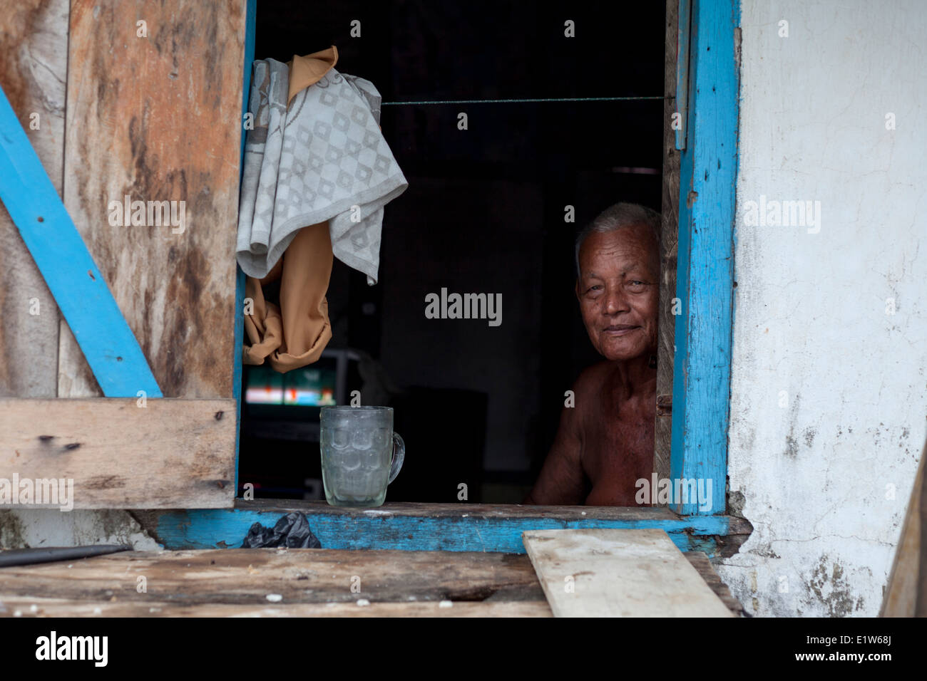 Ein Mann sitzt am Fenster seines Hauses in Bengkulu Stadt, Sumatra, Indonesien. Stockfoto