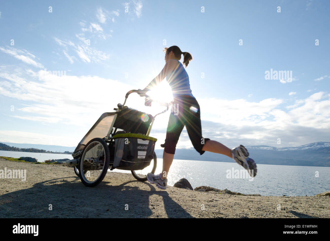 Eine Frau joggt am Ufer des Okanagan Lake mit ihrem Baby in einer Kindertrage Stockfoto