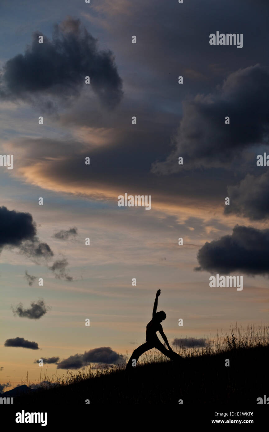 Eine junge Frau praktizieren Yoga auf einem Hügel über der Stadt von Canmore, AB Stockfoto