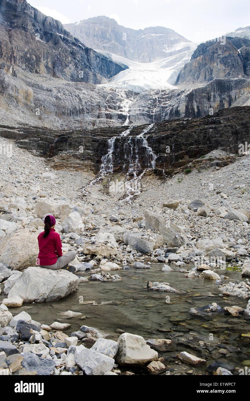 Ein Wanderer sitzt auf einem Felsen neben einem Poolwasser durch den Stanley-Gletscher gespeist. Rauchen Sie in der Nähe ein Lauffeuer hängen über den Bergen. Modell Stockfoto