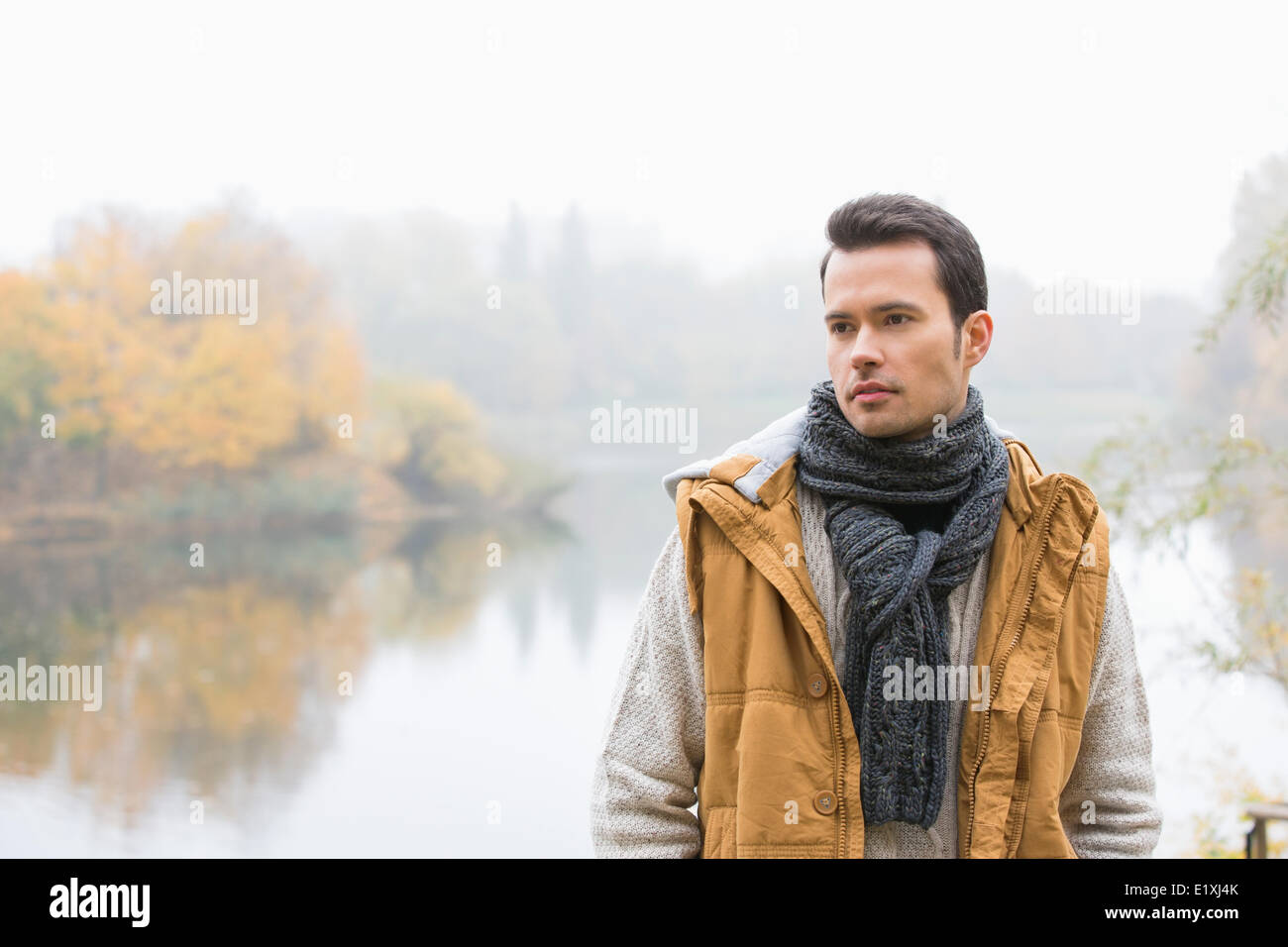 Nachdenklicher junger Mann in warme Kleidung stehend gegen See Stockfoto