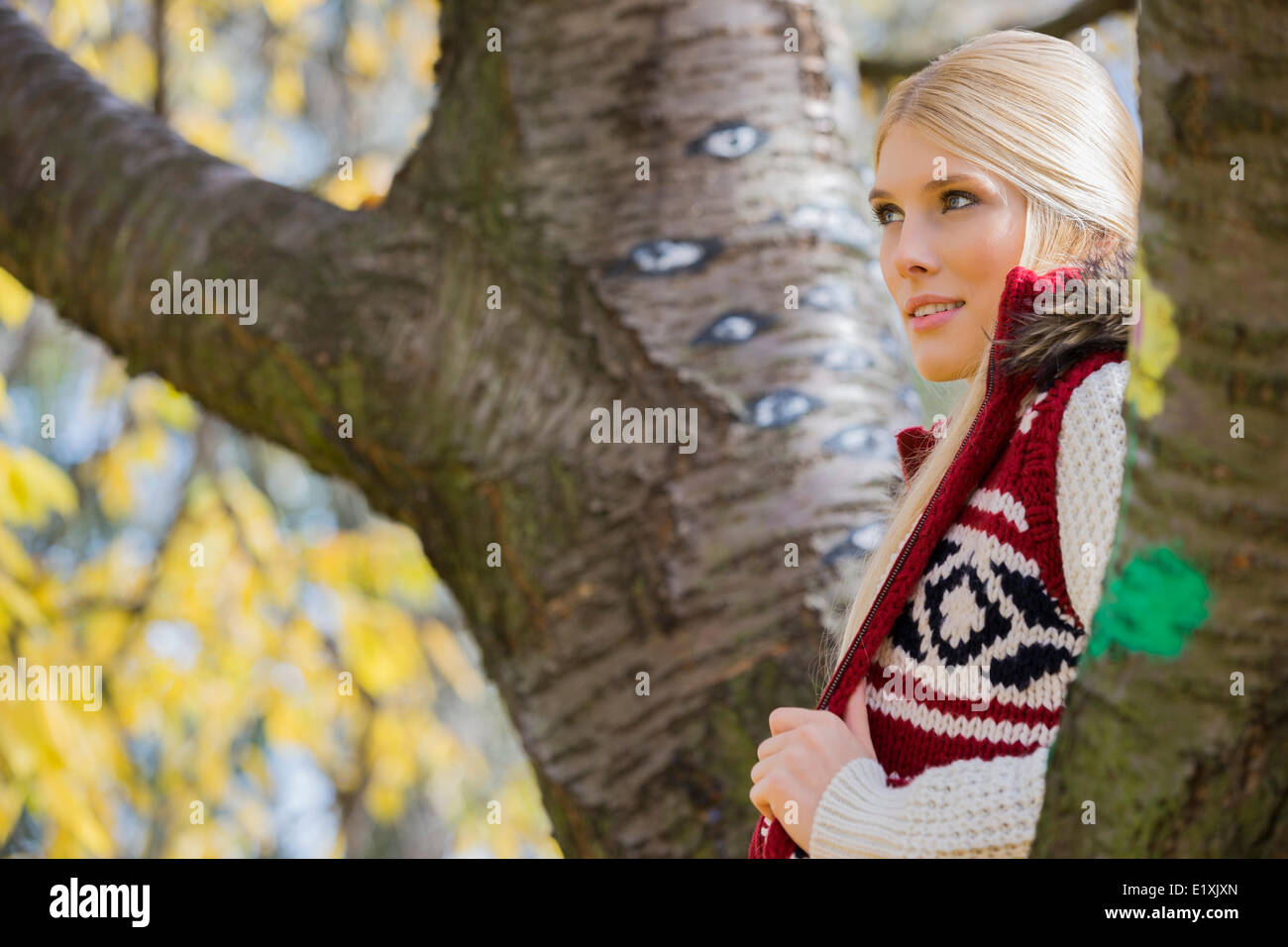 Nachdenkliche junge Frau in warme Kleidung stehen in der Nähe von Bäumen im park Stockfoto