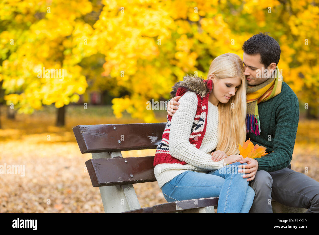 Liebevoller junger Mann umarmt schüchterne Frau auf Parkbank im Herbst Stockfoto