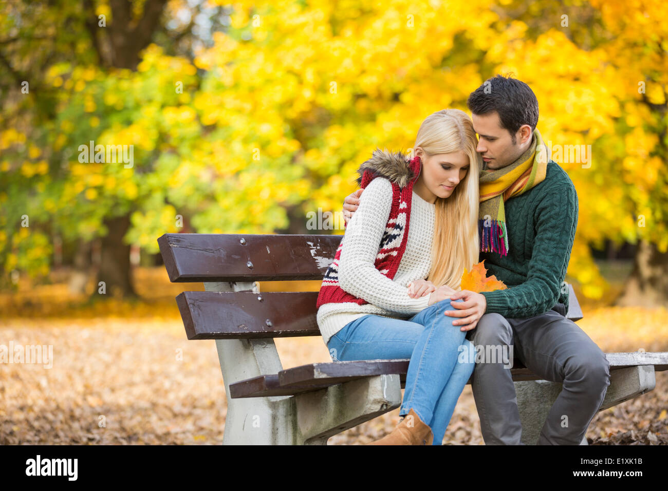 Leidenschaftlicher junger Mann umarmt schüchterne Frau auf Parkbank im Herbst Stockfoto