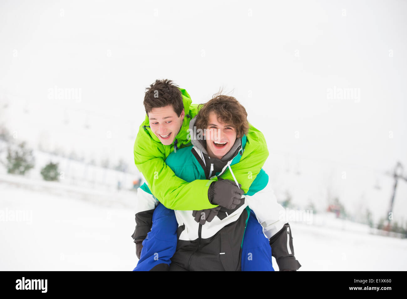 Junge männliche Freunde genießen Huckepack Reiten im Schnee Stockfoto