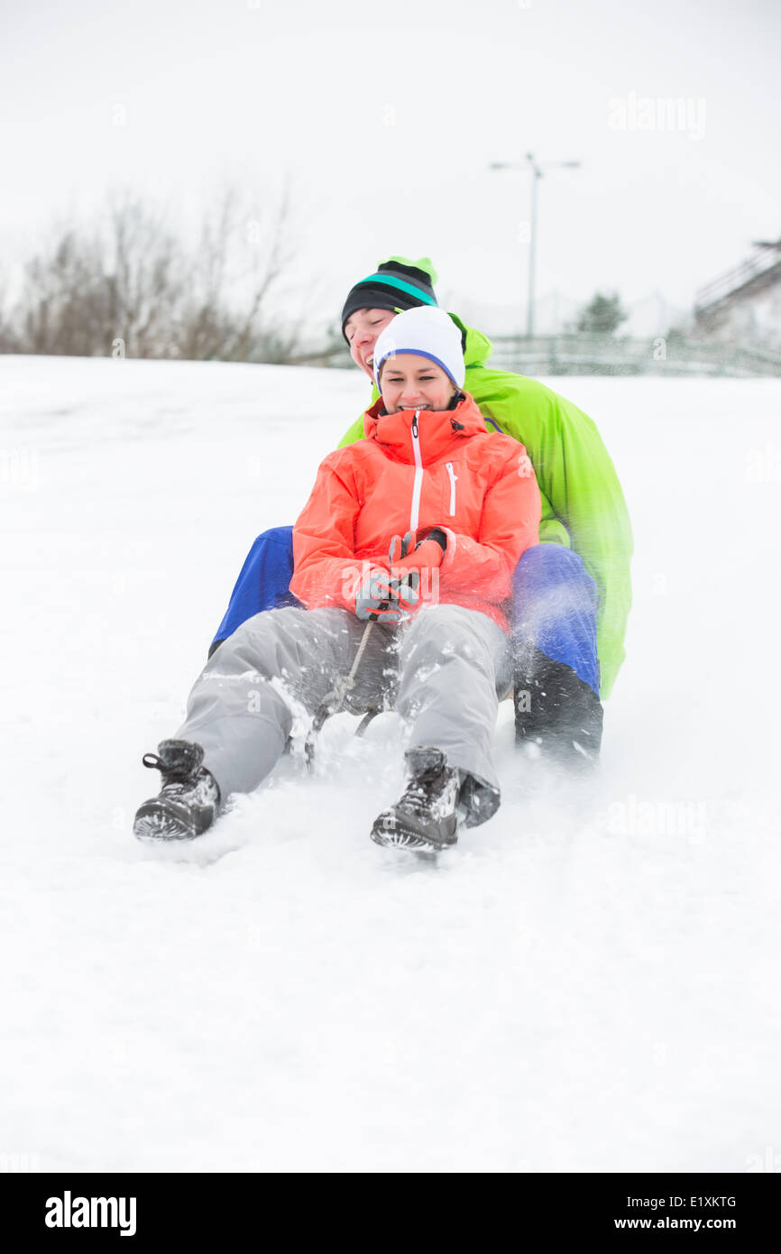 Voller Länge des jungen Paares auf Schnee Rodeln bedeckt land Stockfoto