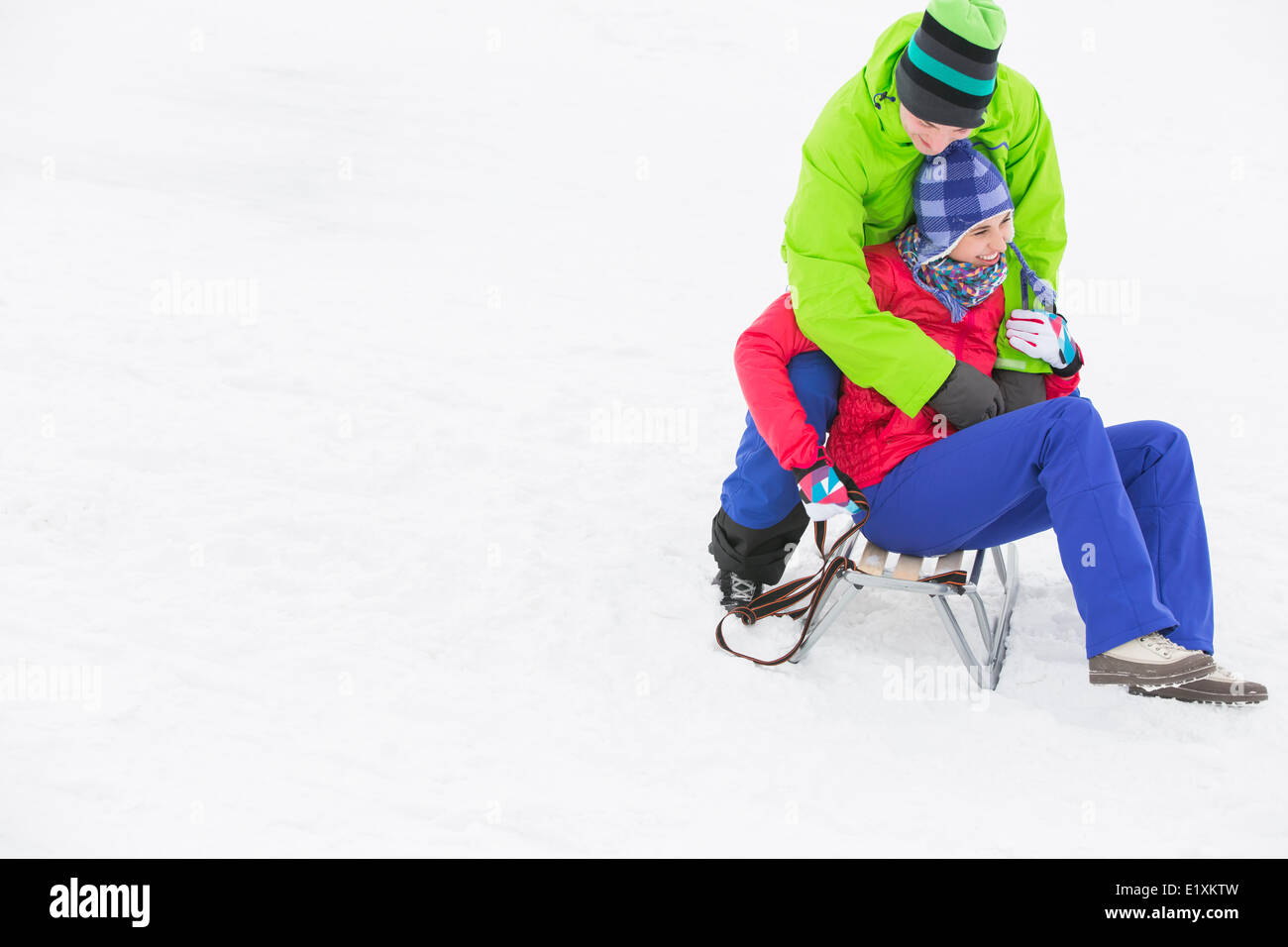 Junger Mann umfassenden Frau auf Schlitten im Schnee Stockfoto