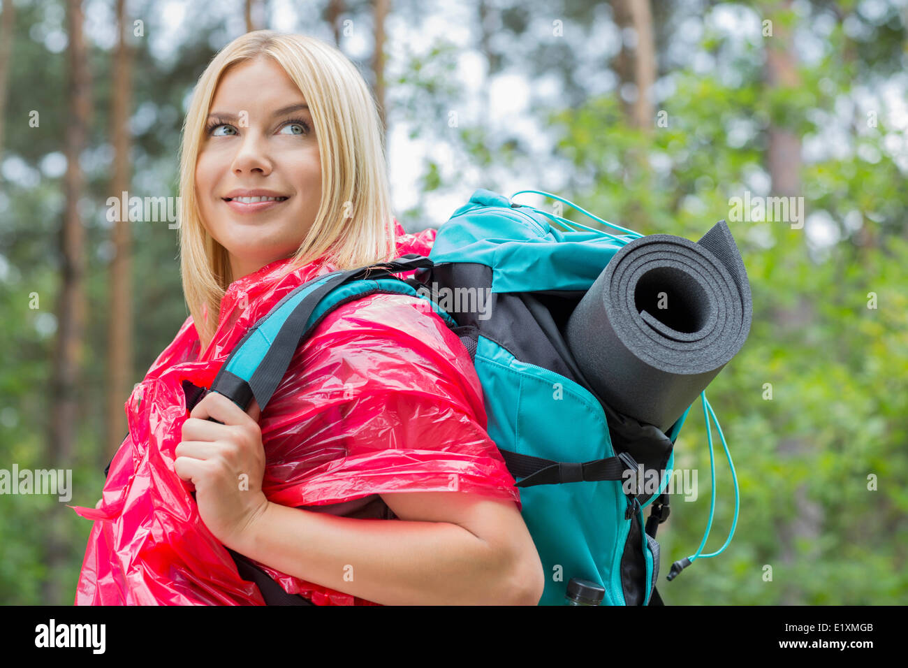 Seitenansicht lächelnde weibliche Backpacker in Regenmantel Wegschauen am Wald Stockfoto