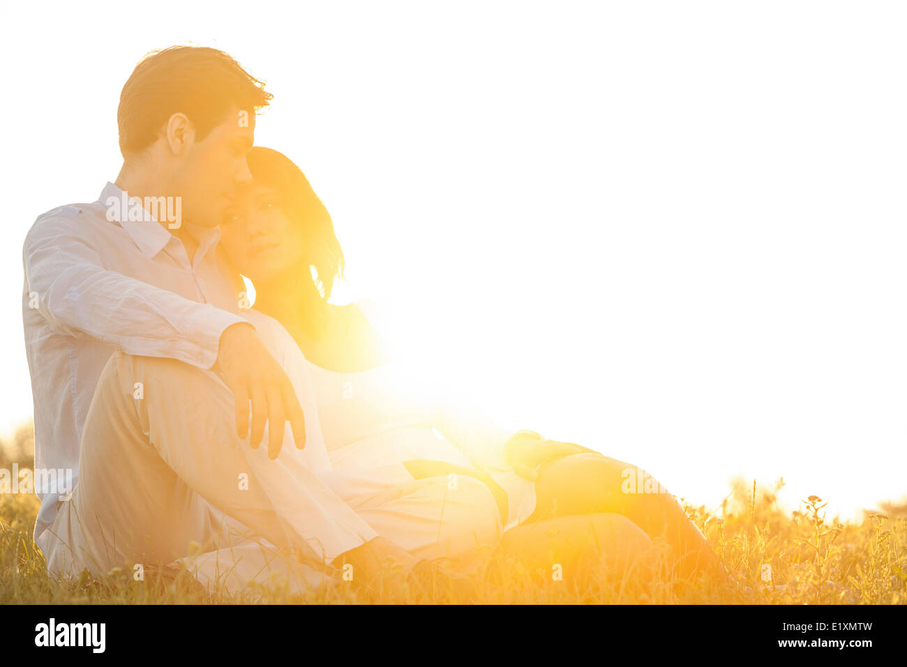 Junges Liebespaar sitzen auf dem Rasen im Park gegen den klaren Himmel Stockfoto