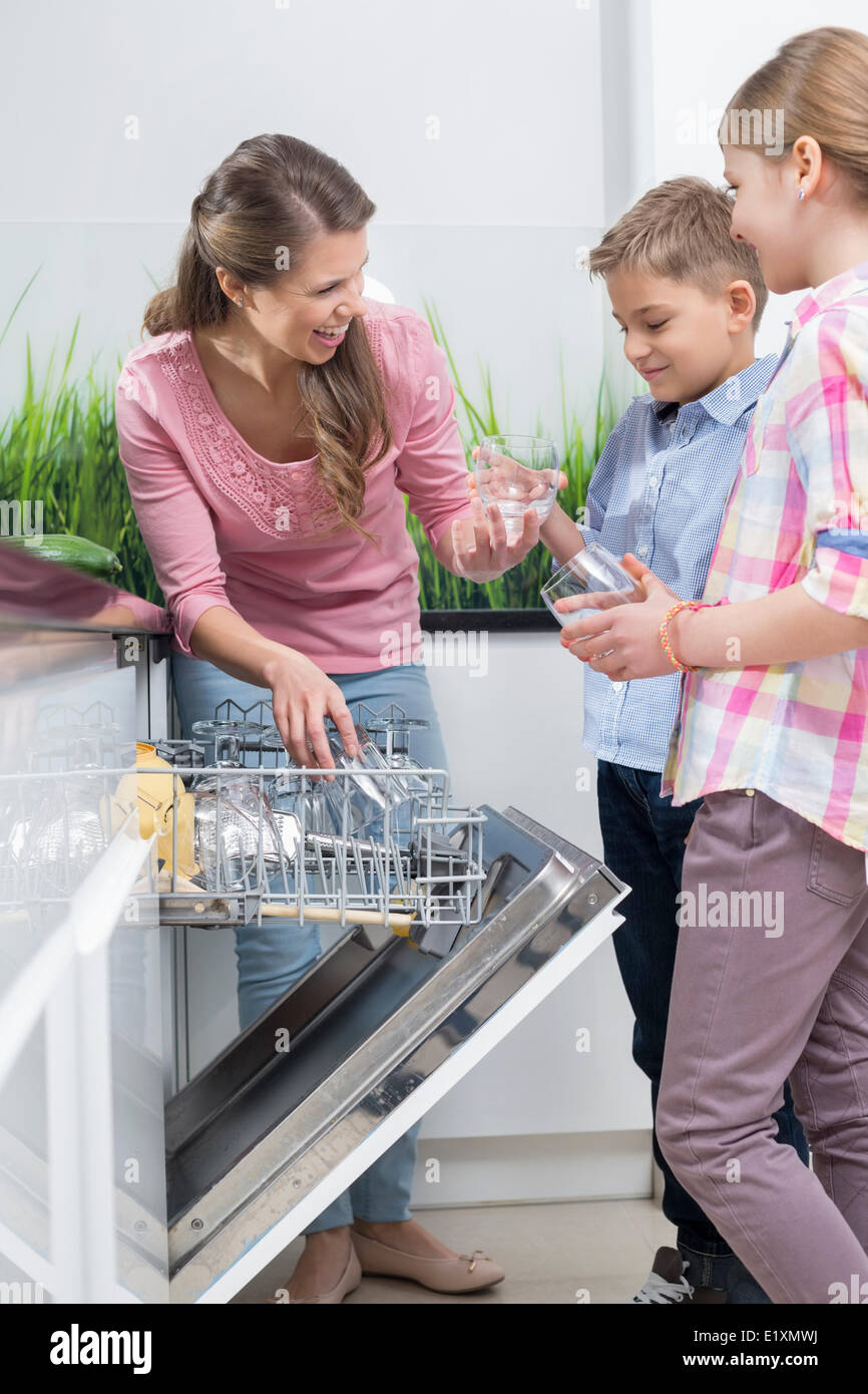 Glückliche Mutter und Kinder platzieren Gläser in Spülmaschine Stockfoto