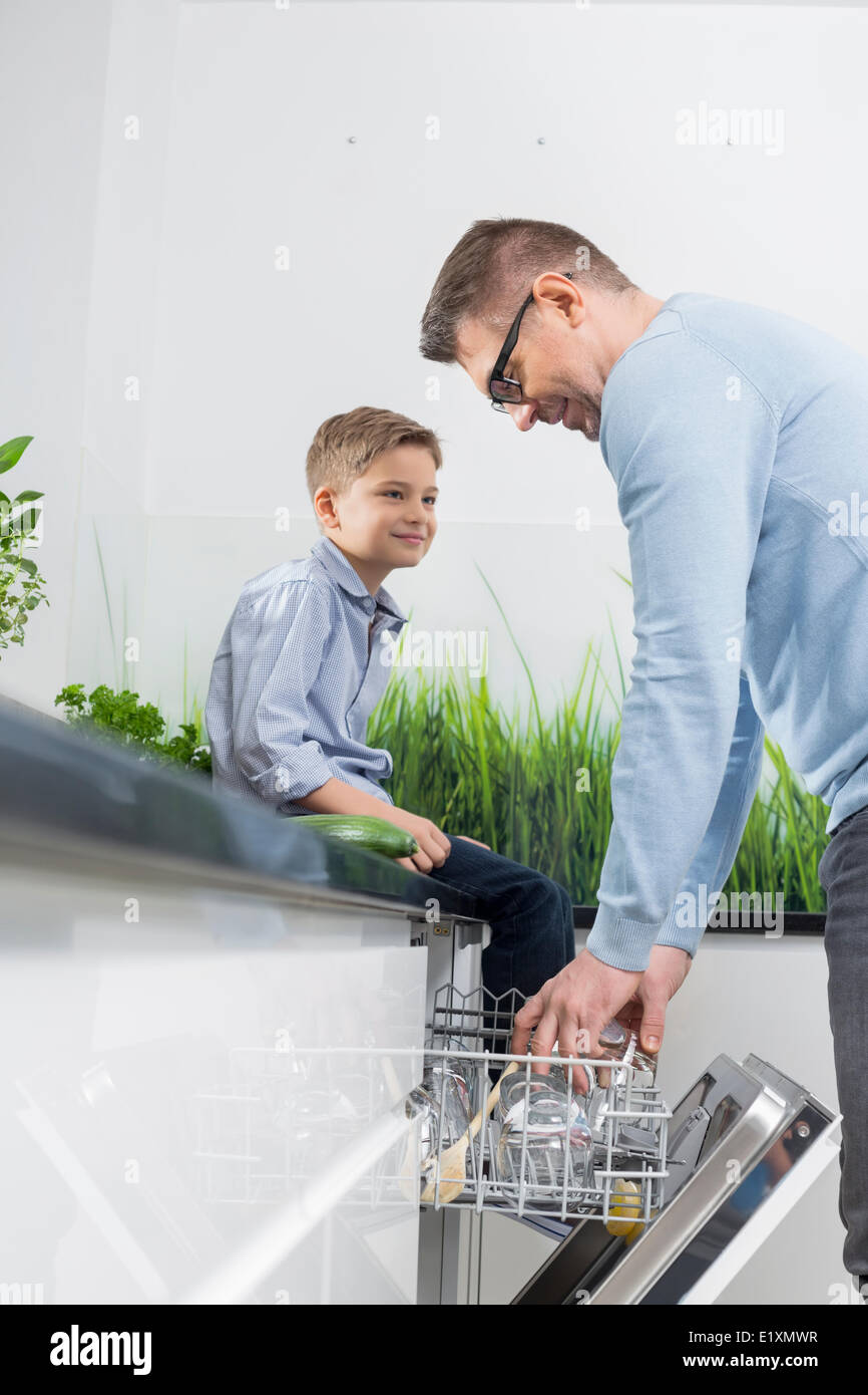 Junge Blick auf Vater Platzierung Glas im Geschirrspüler in der Küche Stockfoto