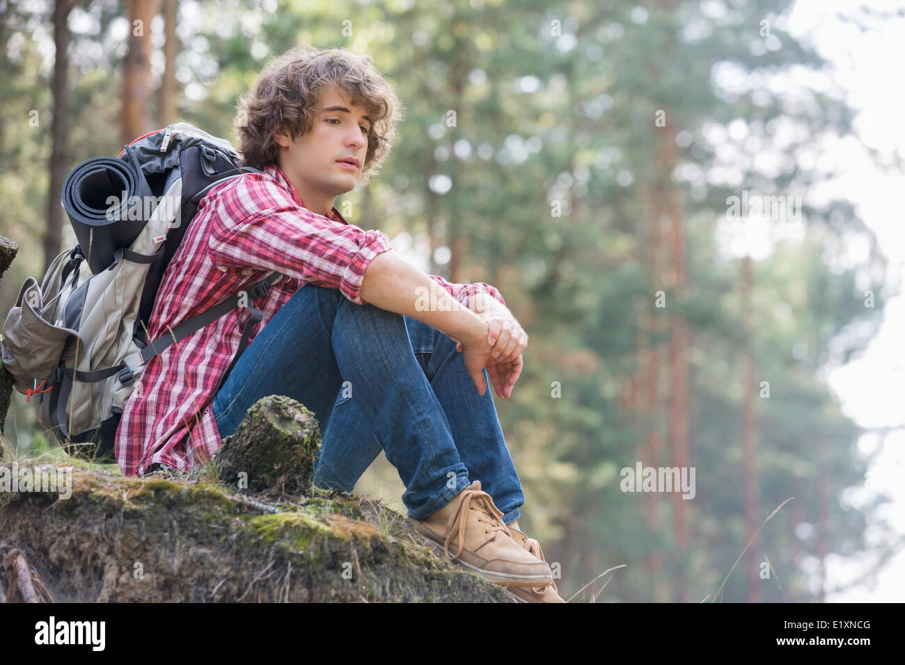 Voller Länge der nachdenklichen männlichen Backpacker entspannend auf Felsen im Wald Stockfoto