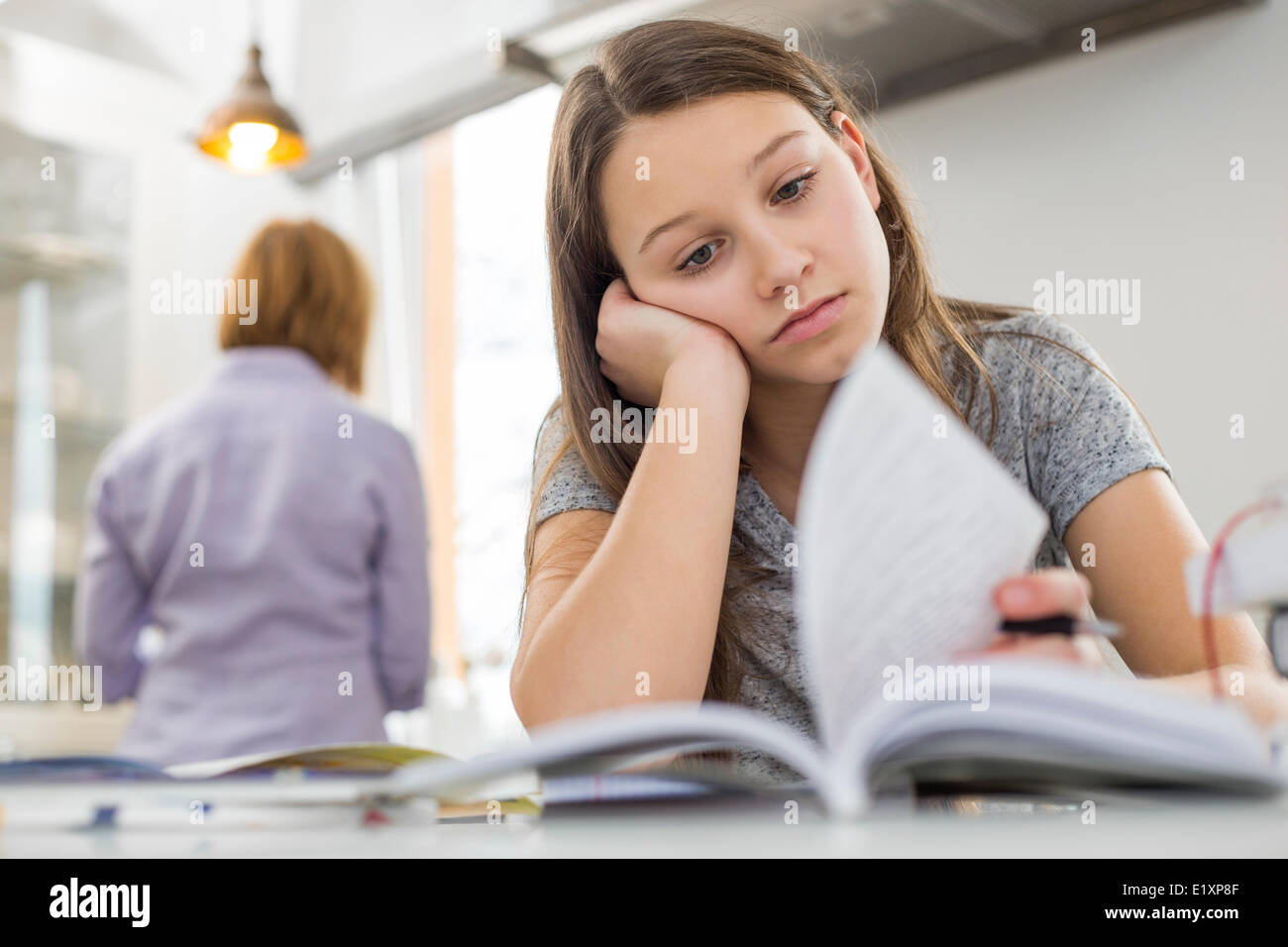 Gelangweilt Mädchen studieren am Tisch mit Mutter im Hintergrund stehen Stockfoto