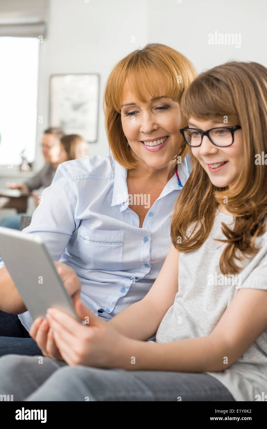 Glückliche Mutter und Tochter mit tablet-PC mit Familie sitzt im Hintergrund zu Hause Stockfoto